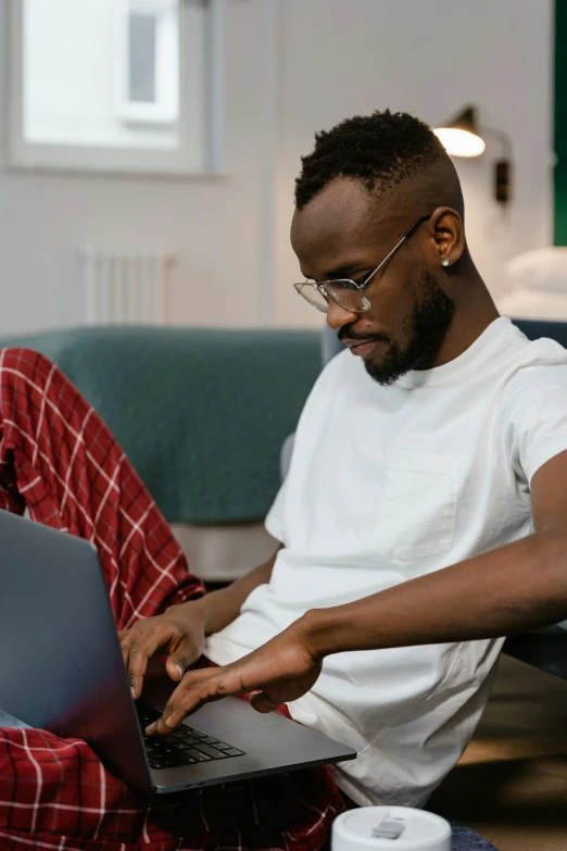 a man sitting on a couch using a laptop, trending on pexels, afrofuturism, wearing a white button up shirt, non-binary, bending down slightly, a young man