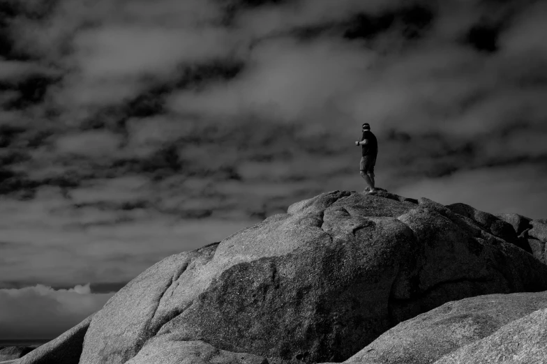 a black and white po of a man standing on the top of a large rock