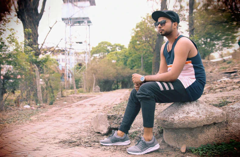 a man sitting on a rock on a dirt road, an album cover, inspired by Saurabh Jethani, pexels contest winner, wearing adidas clothing, in a city park, profile image, sleeveless