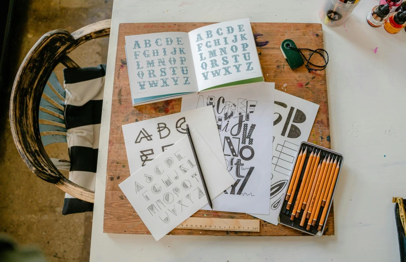 a wooden cutting board sitting on top of a table, a screenprint, by Jessie Algie, unsplash, letterism, drawing sketches on his notebook, uppercase letter, grid of styles, thumbnail