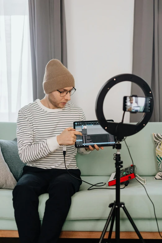 a man sitting on a couch holding a camera, ring light, tiktok video, screen light, with a round face