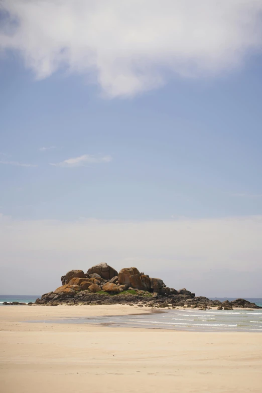 a man riding a surfboard on top of a sandy beach, in the distance is a rocky hill, somalia, round-cropped, an island