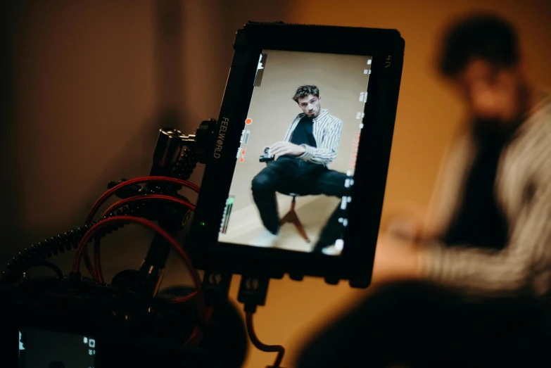 a man sitting on a chair in front of a camera, a picture, unsplash, video art, rectangle, cinematic outfit photo, colour photograph, close up to the screen