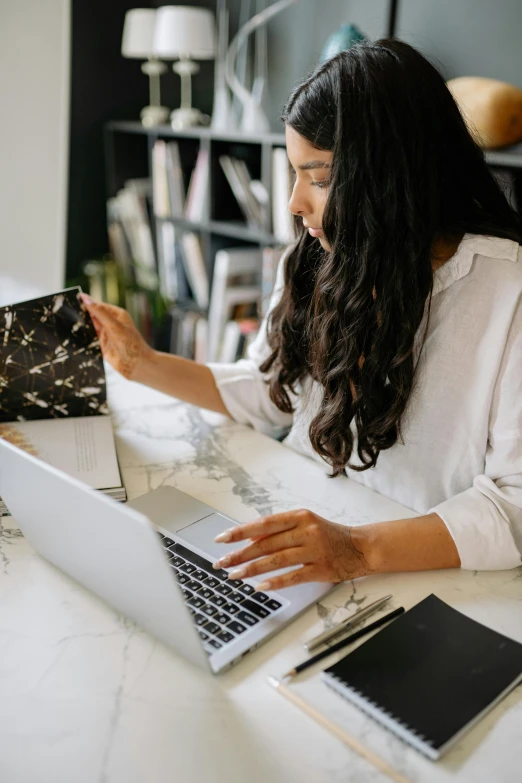 a woman sitting at a table working on a laptop, by Julia Pishtar, pexels contest winner, ornate designs on desk, white map library, black, thumbnail