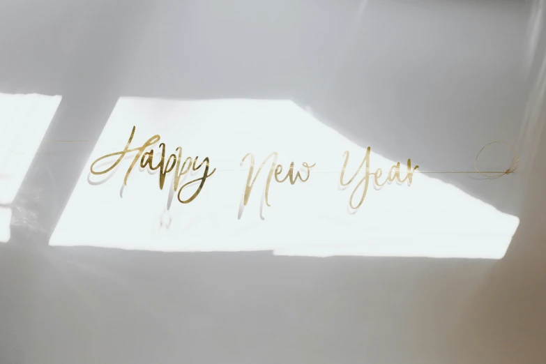 a piece of paper with the words happy new year written on it, by Emma Andijewska, trending on unsplash, gold decoration, glossy white metal, transparent glass surfaces, mid-twenties