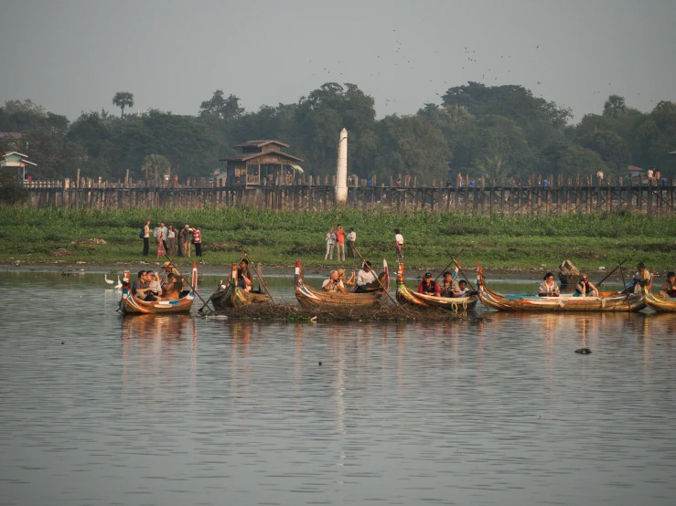 a group of people riding canoes down a river, hurufiyya, temple in the distance, maintenance photo, myanmar, fish flocks