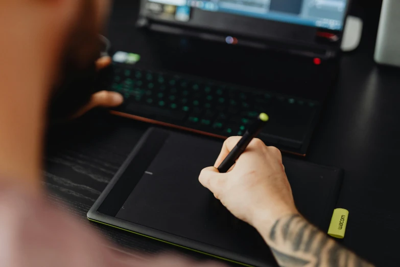 a person sitting at a desk with a laptop and a pen, a drawing, green and black colors, draw with wacom tablet, with a laptop on his lap, wlop and ross thran