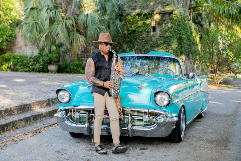 a man playing saxophone in front of an old blue car