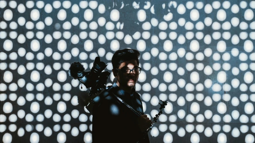 a man with a gun standing in front of a wall, an album cover, unsplash, bauhaus, studio diffuse lights, holding a scepter, holding a big camera, cinematic lights