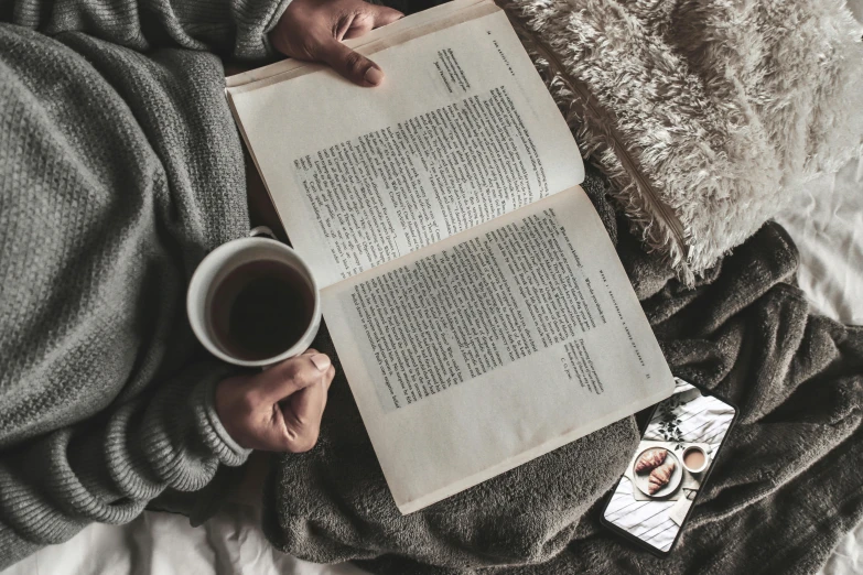 a person laying on a bed with a book and a cup of coffee, a photo, by Lucia Peka, pexels contest winner, cold as ice! 🧊, vintage photo, background image, selfie photo