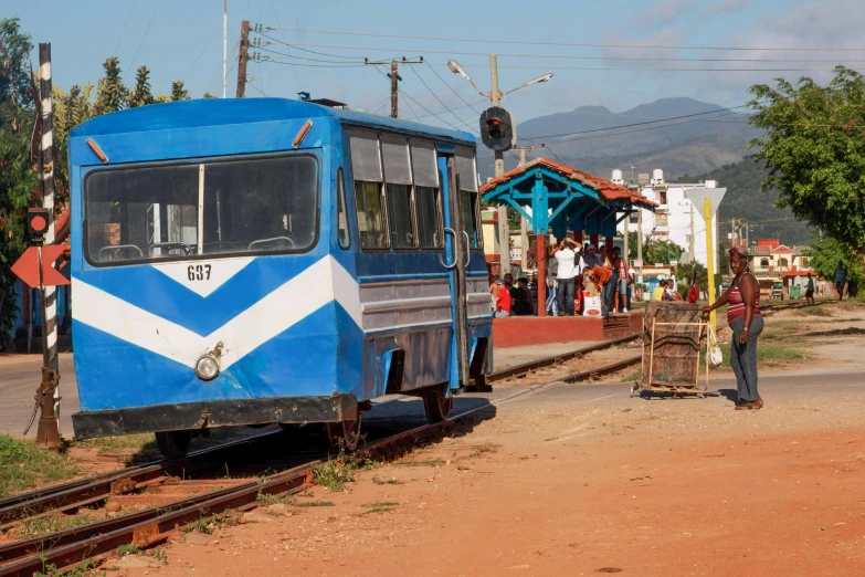 blue train on the railroad tracks near a road with pedestrians