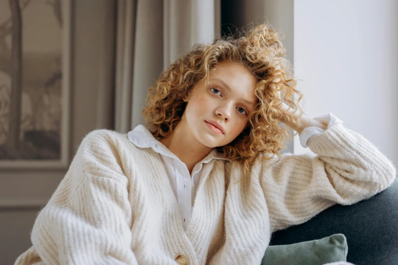 a woman with curly hair sitting on a couch, by Emma Andijewska, trending on pexels, renaissance, white sweater, eleven/millie bobbie brown, handsome girl, blonde reddish hair