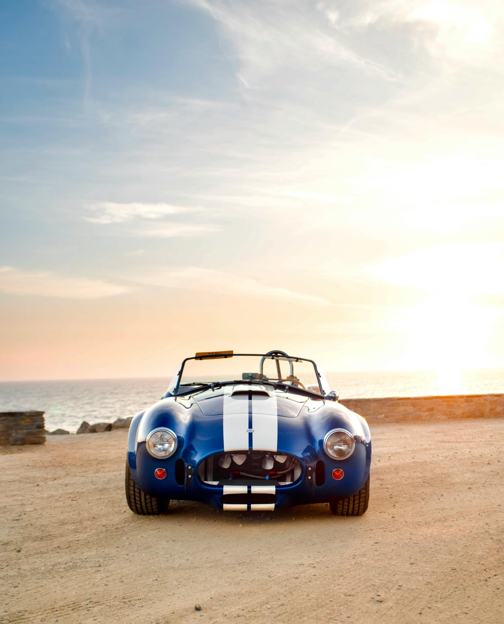 the sports car is parked on the sand in front of the ocean