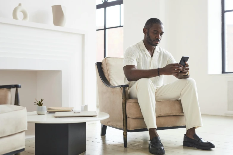 a man sitting in a chair looking at his cell phone, curated collections, white hue, minimalist furniture, ( ( dark skin ) )