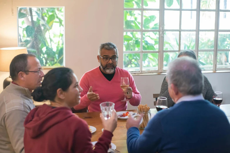 a group of people sitting around a wooden table, inspired by Francis Souza, pexels contest winner, holding a glass of wine, avatar image, colombian, facing away