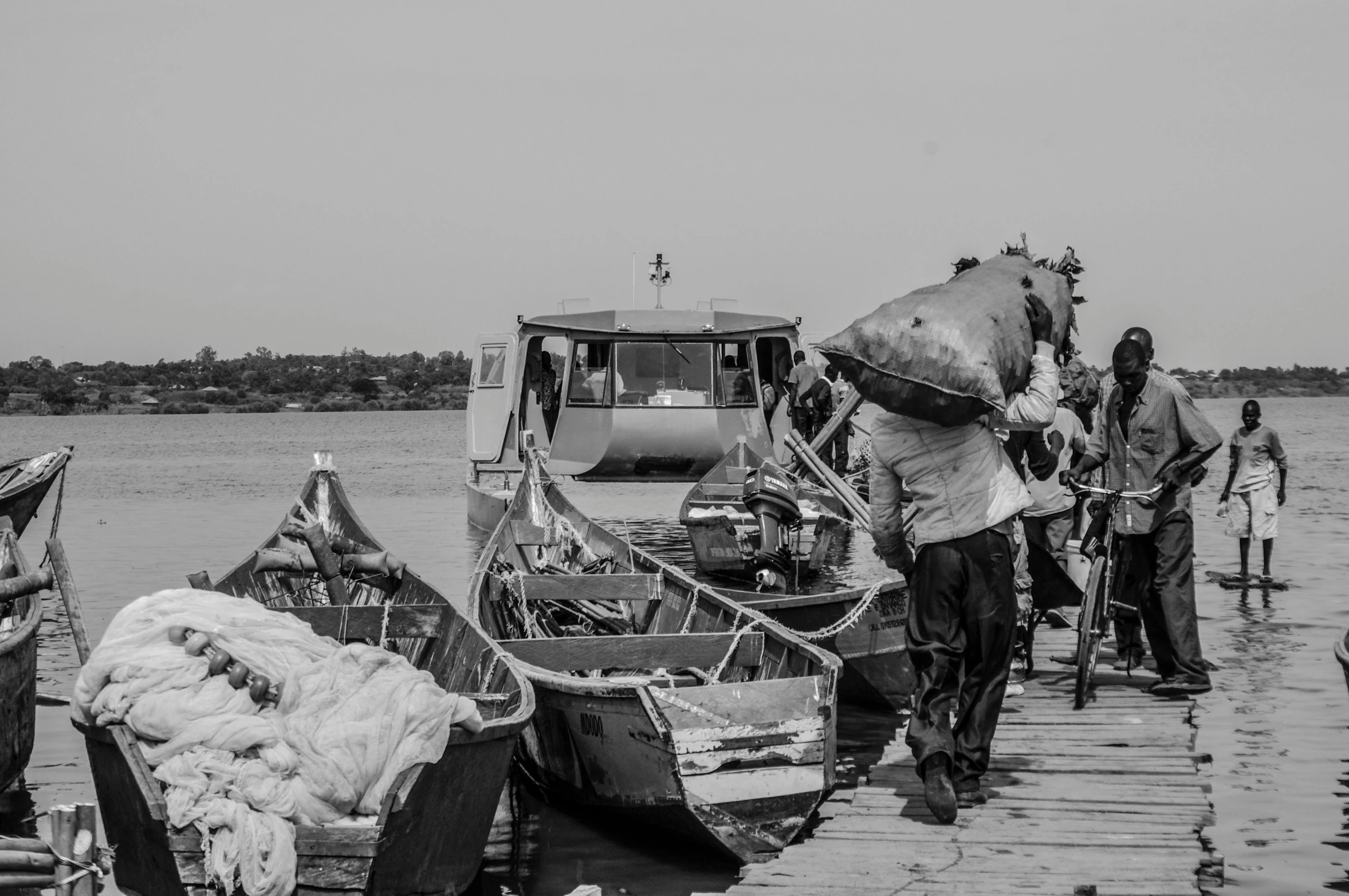 a group of people standing on a dock next to a body of water, a black and white photo, by Ceferí Olivé, pexels contest winner, process art, fishing boats, carrying big sack, four legged, with a bunch of stuff