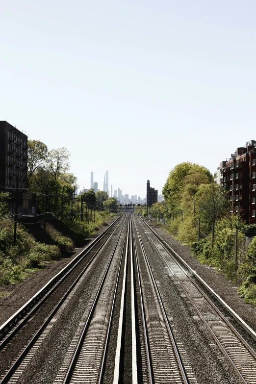 a view of a train track with buildings in the background, by Washington Allston, unsplash, clear skies in the distance, new york zoo in the background, pitchfork, plain stretching into distance