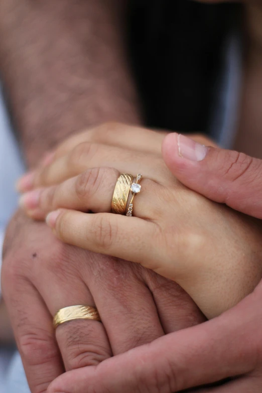 a close up of a person holding a person's hand, by Nina Hamnett, gold rings, inlaid with gold, happy couple, finely textured