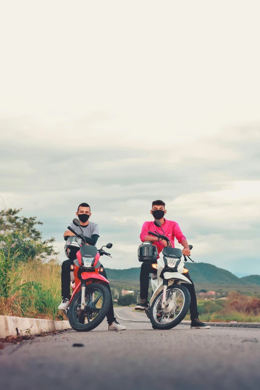 two men standing next to motorcycles on a road, a picture, unsplash, pink, in style of thawan duchanee, avatar image, scenic view