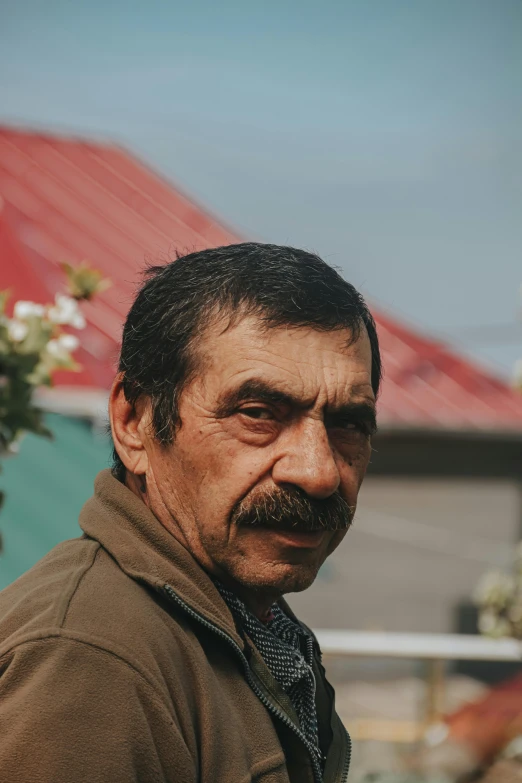 a man with a mustache standing in front of a building, wrinkled face, romanian, profile image, standing in a township street