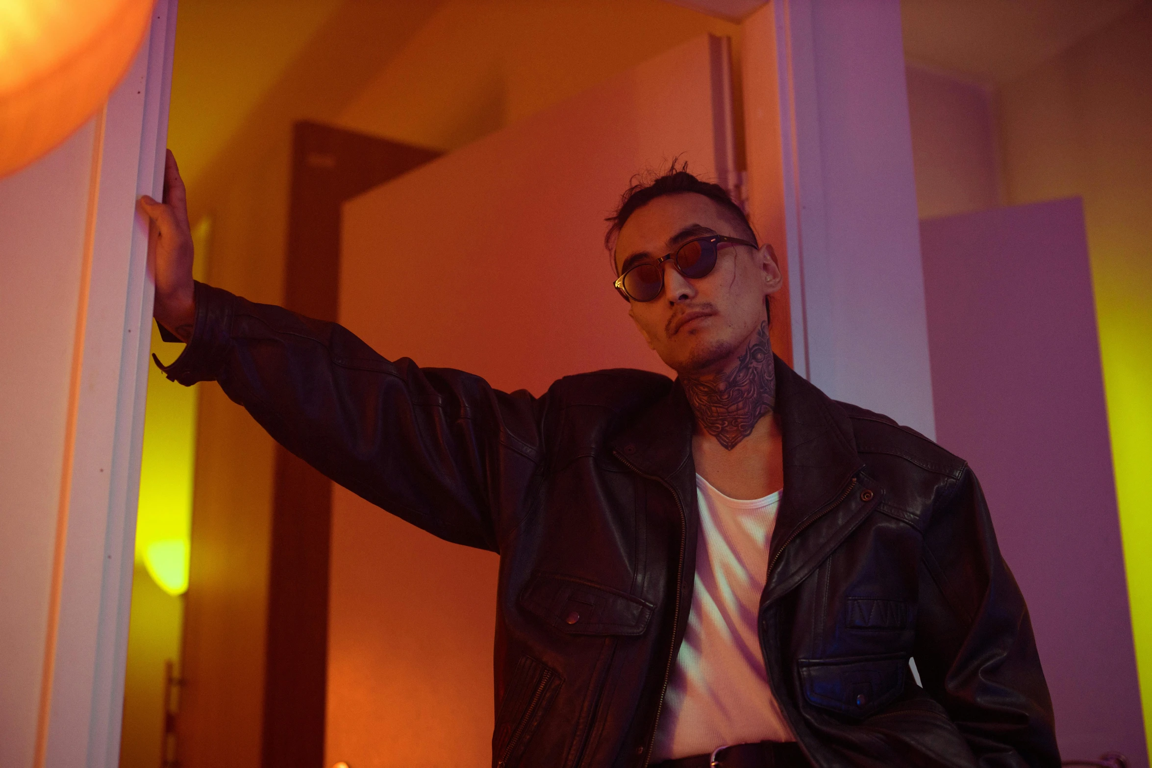 a man wearing a leather jacket and round sunglasses pointing his finger