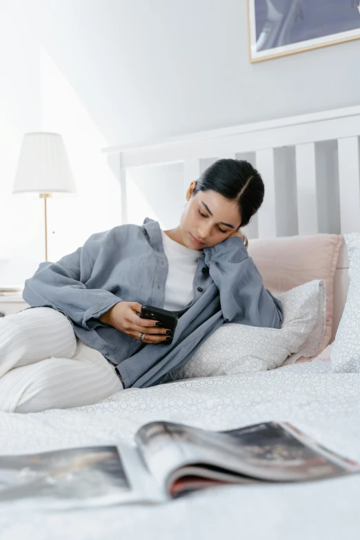 a woman sitting on a bed reading a book, trending on pexels, happening, wearing sweatshirt, checking her phone, annoyed, grey robe