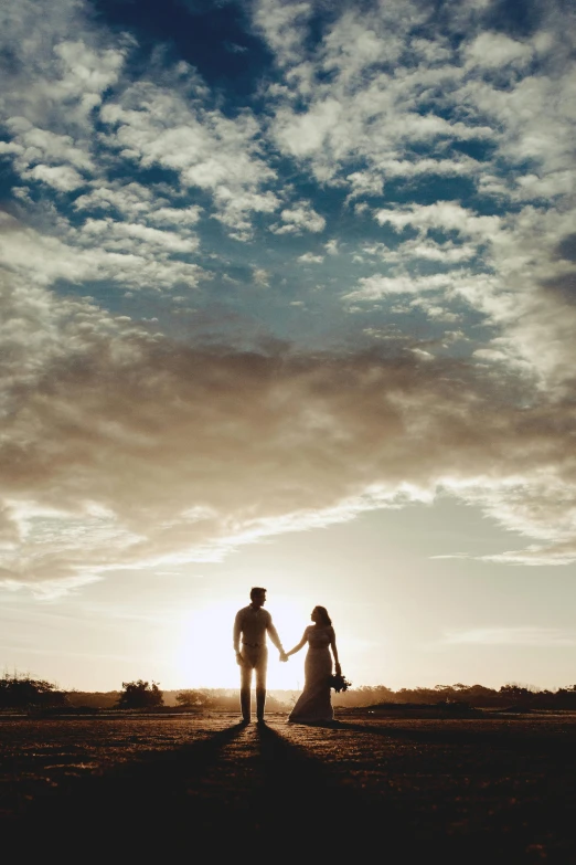 a couple holding hands as the sun sets, by Gwen Barnard, unsplash contest winner, “ iron bark, wedding photo, blue skies, distant full body view