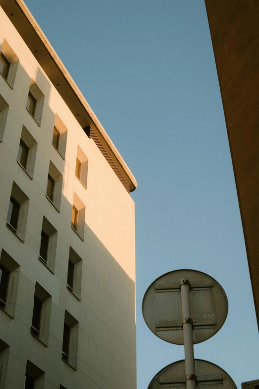 a street light sitting next to a tall building, inspired by André Kertész, unsplash contest winner, postminimalism, cloudless sky, golden hour hues, french architecture, rounded architecture