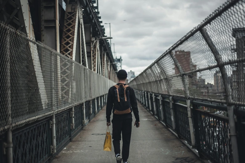 a person walking across a bridge carrying a bag, pexels contest winner, brooklyn, thin young male, learning, ignant