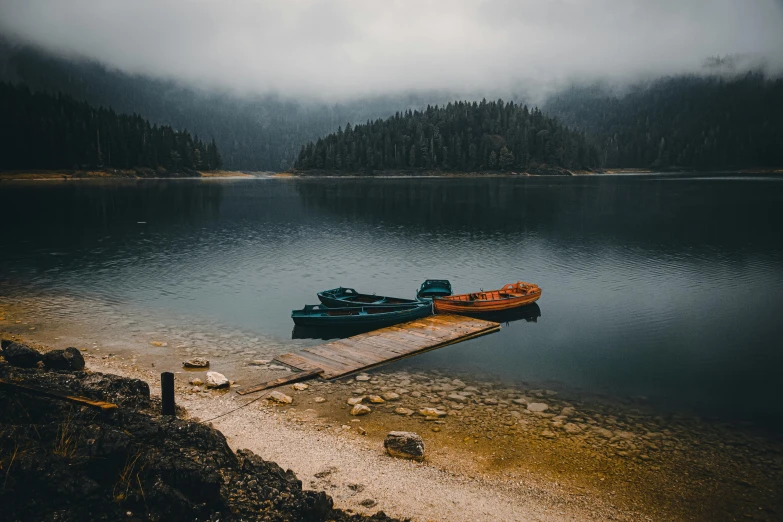 a couple of boats sitting on top of a lake, by Emma Andijewska, pexels contest winner, overcast gray skies, 90s photo, leaked photo, mountain lakes