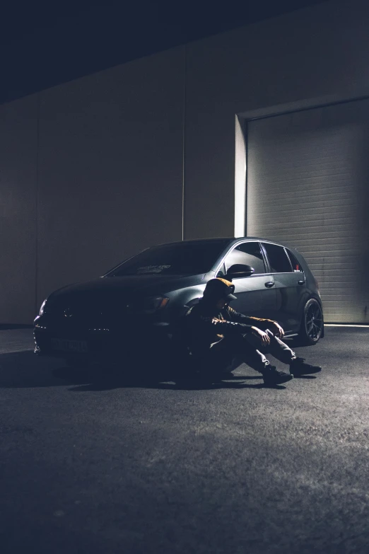 a person laying on the ground next to a car, inspired by Elsa Bleda, pexels contest winner, realism, vantablack chiaroscuro, samurai vinyl wrap, confident stance, sitting down