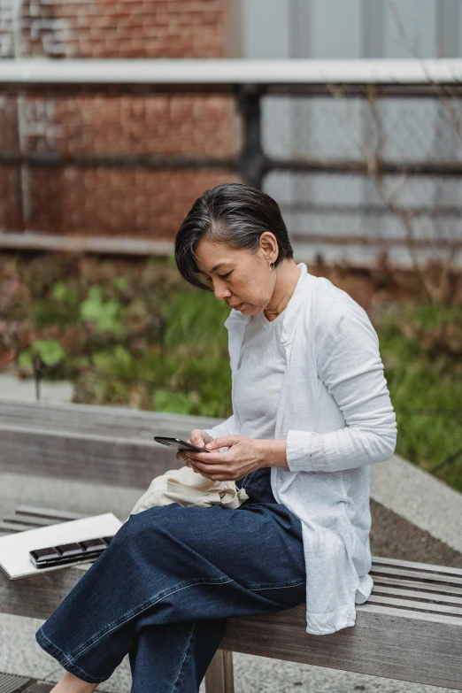 a woman sitting on a bench looking at her cell phone, happening, bao pham, wearing a linen shirt, dwell, ignant