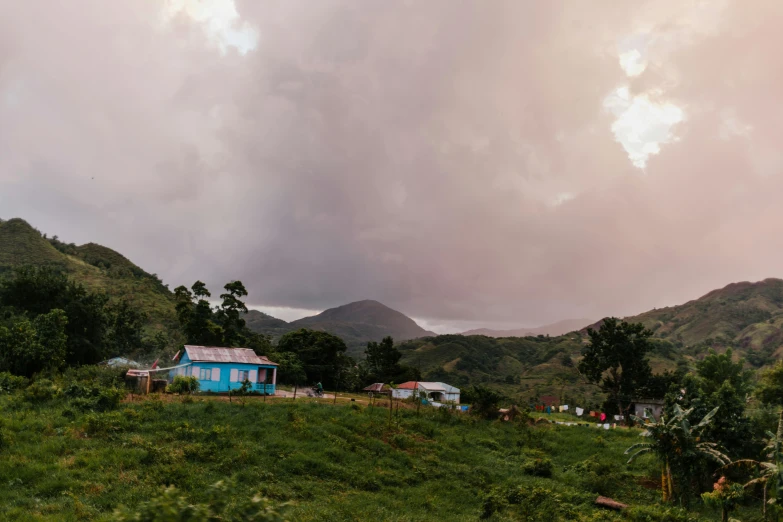 a blue house sitting on top of a lush green hillside, by Jessie Algie, pink storm clouds, tribe huts in the jungle, golden hour photo, panoramic