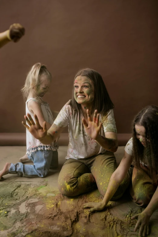 a group of children sitting on the ground covered in paint, inspired by Helen Frankenthaler, shutterstock contest winner, interactive art, girl in studio, brown, cottagecore hippie, woman
