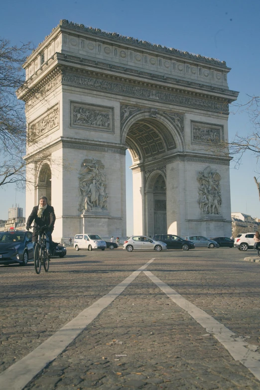 a man riding a bike down a street next to a tall arch, cinematic paris, photograph, b - roll, illustration »