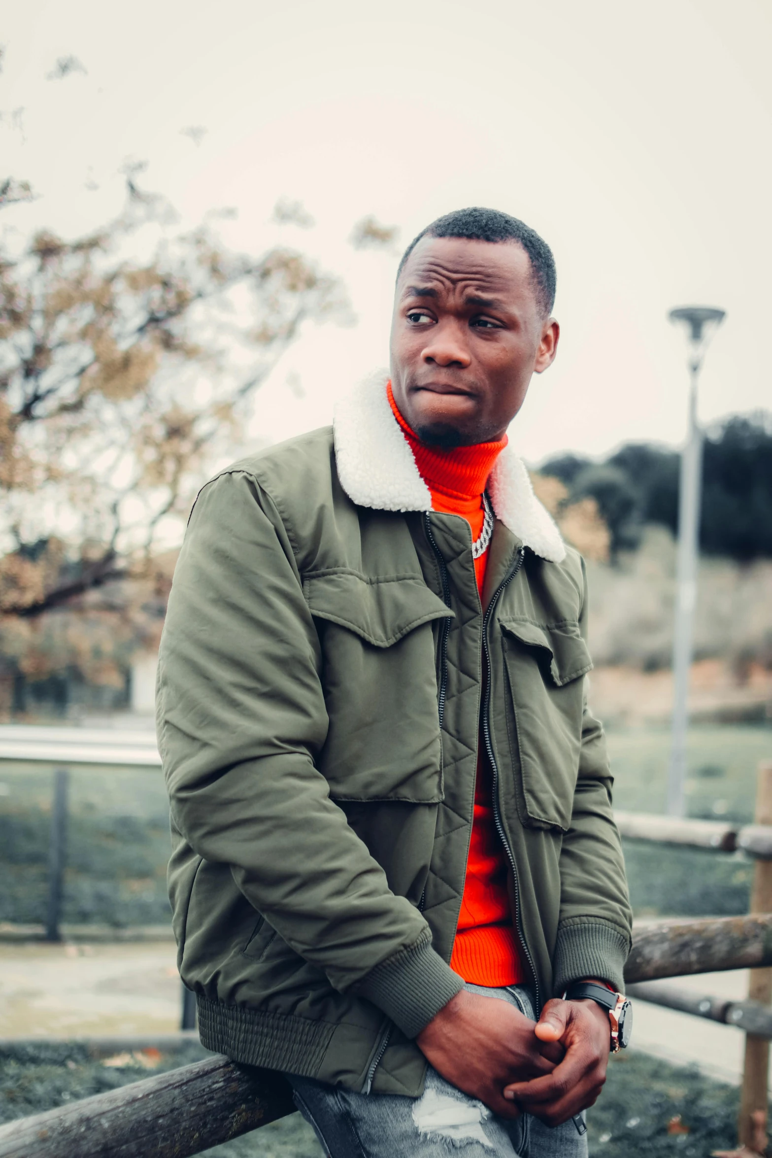 a man sitting on top of a wooden fence, an album cover, inspired by Theo Constanté, pexels contest winner, les nabis, wearing a turtleneck and jacket, disappointed, ( ( dark skin ) ), wide forehead