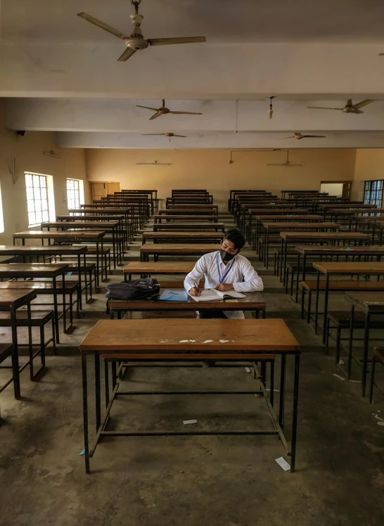 a man sitting at a desk in a classroom, an album cover, pexels, bengal school of art, in a desolate, medical lab, thumbnail, ap news photograph
