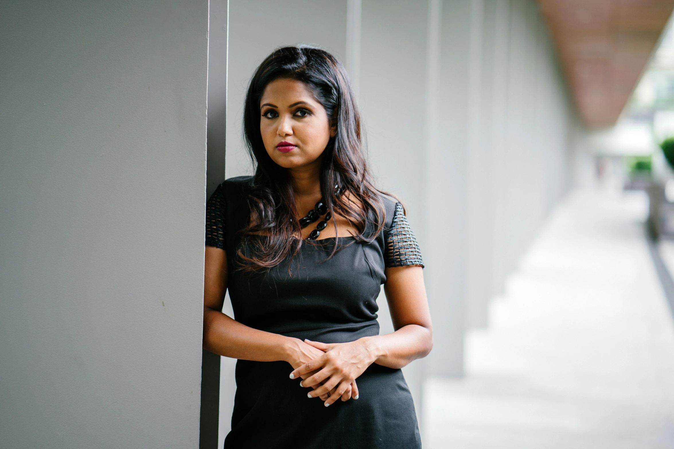 a woman in a black dress leaning against a wall, hurufiyya, bold serious expression, nivanh chanthara, square, professional image