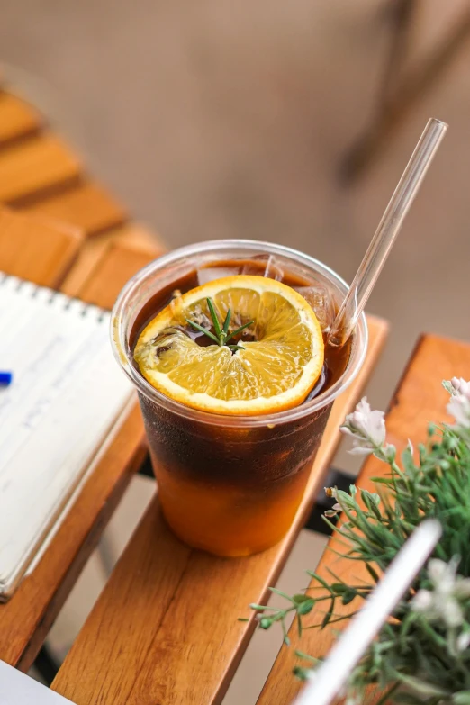 a drink sitting on top of a wooden table next to a laptop, by Reuben Tam, unsplash, photorealism, iced tea glass, orange halo, straw, yellow charcoal