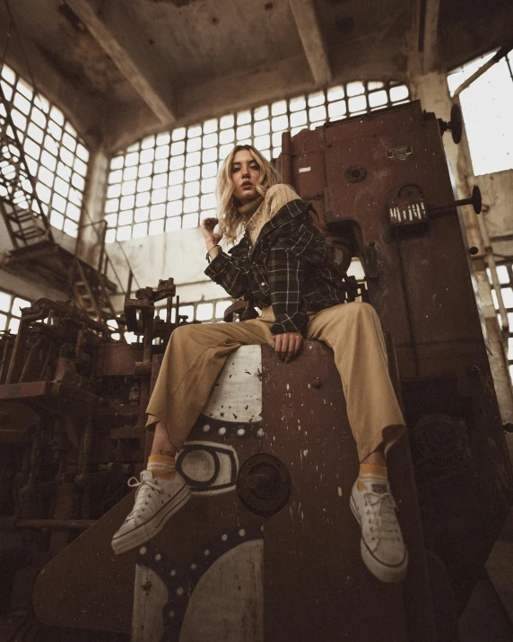 a woman sitting on top of a piece of luggage, inspired by Elsa Bleda, trending on pexels, graffiti, stood in a factory, brown pants, dieselpunk look, non binary model