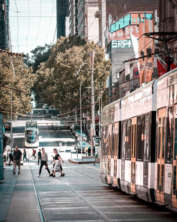 a train traveling down a city street next to tall buildings, by Anna Findlay, pexels contest winner, happening, north melbourne street, people walking around, square, trams ) ) )