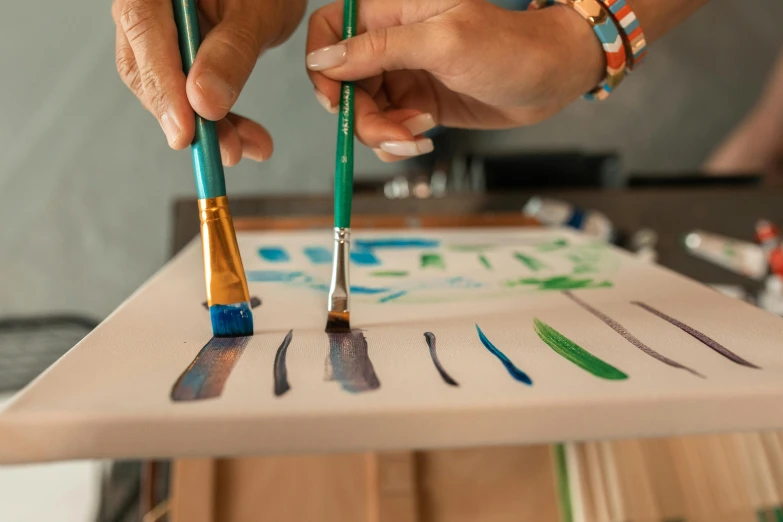 a close up of a person painting on a piece of paper, greens and blues, holding paintbrushes, ouchh and and innate studio, on a canva