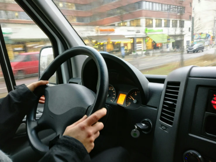 a person driving a car on a city street, hand controlling, microbus, commercially ready, square