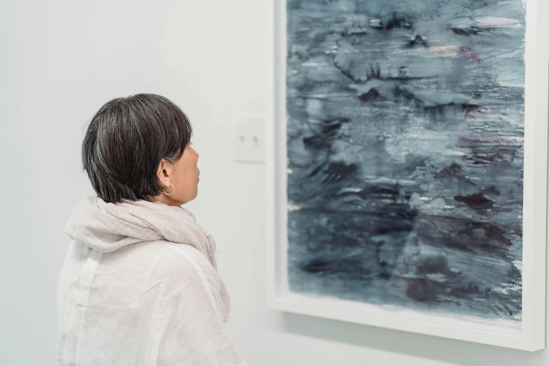 a woman looking at a painting on a wall, inspired by Vija Celmins, trending on unsplash, natsumi mukai artwrok, shades of blue and grey, profile image, worried