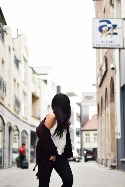 a woman standing on a skateboard on a city street, by Niko Henrichon, happening, long black hair, reykjavik, showing her shoulder from back, cardigan