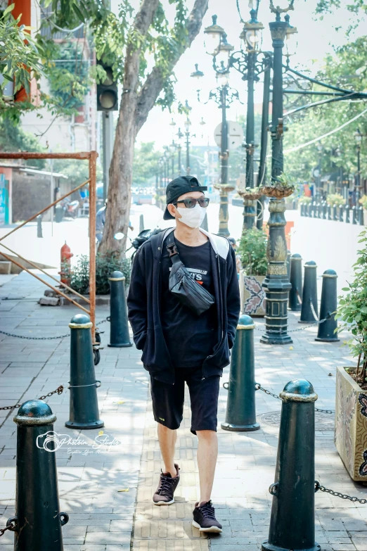 a man with a protective mask walks down a city sidewalk