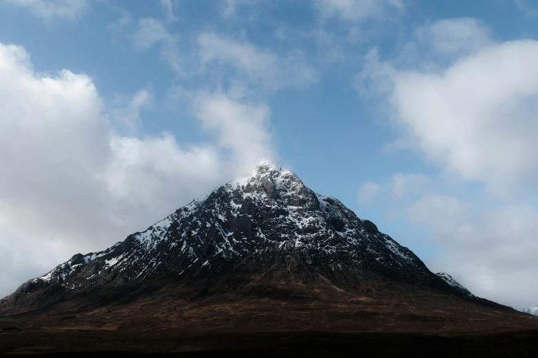 a mountain covered in snow and clouds under a blue sky