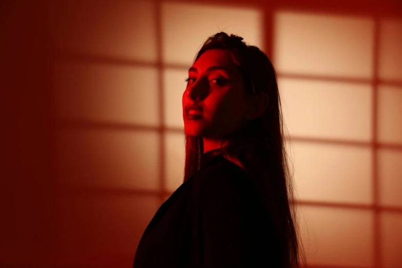 a woman with long hair standing in front of a wall, an album cover, inspired by Elsa Bleda, unsplash, realism, red lighting on their faces, studio backlight, masami suda, portrait of florence pugh