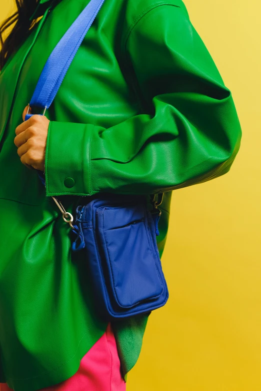 a woman wearing a green jacket and pink pants, an album cover, inspired by Yves Klein, trending on pexels, holding a leather purse, blue and yellow color theme, detail shot, holster