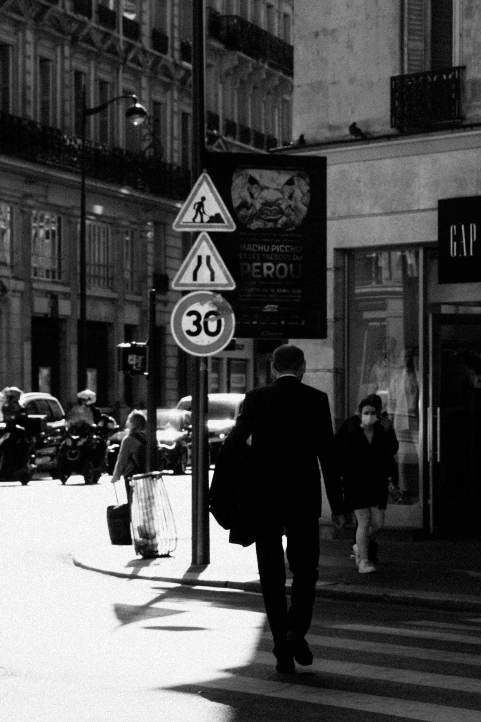 a black and white photo of people walking down a street, a poster, by Jean-Yves Couliou, flickr, traffic signs, man in his 30s, paris 2010, 2 2 nd century!!!!! town street